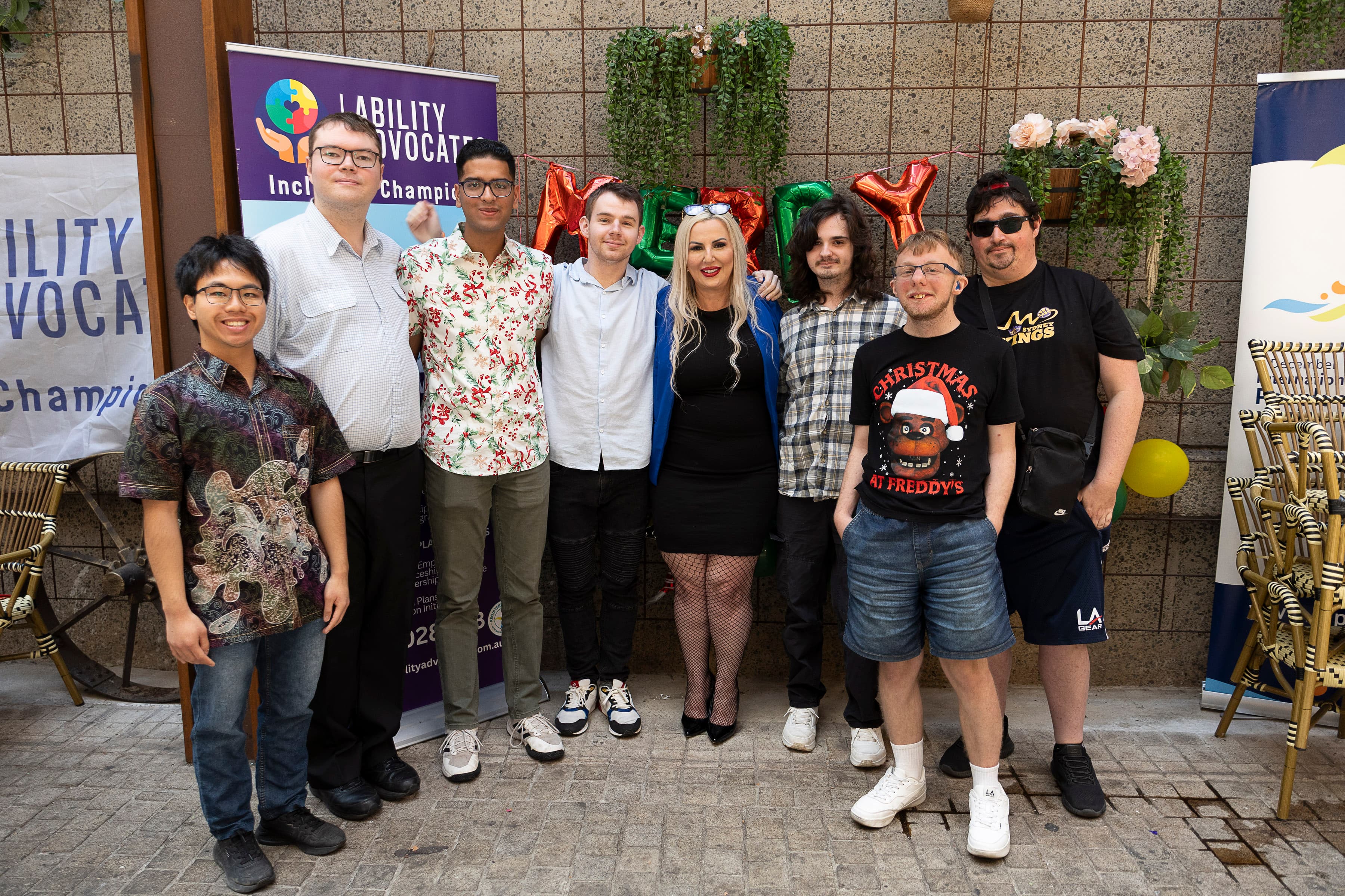 Eight people pose together in front of Ability Advocates banners and festive holiday decorations.