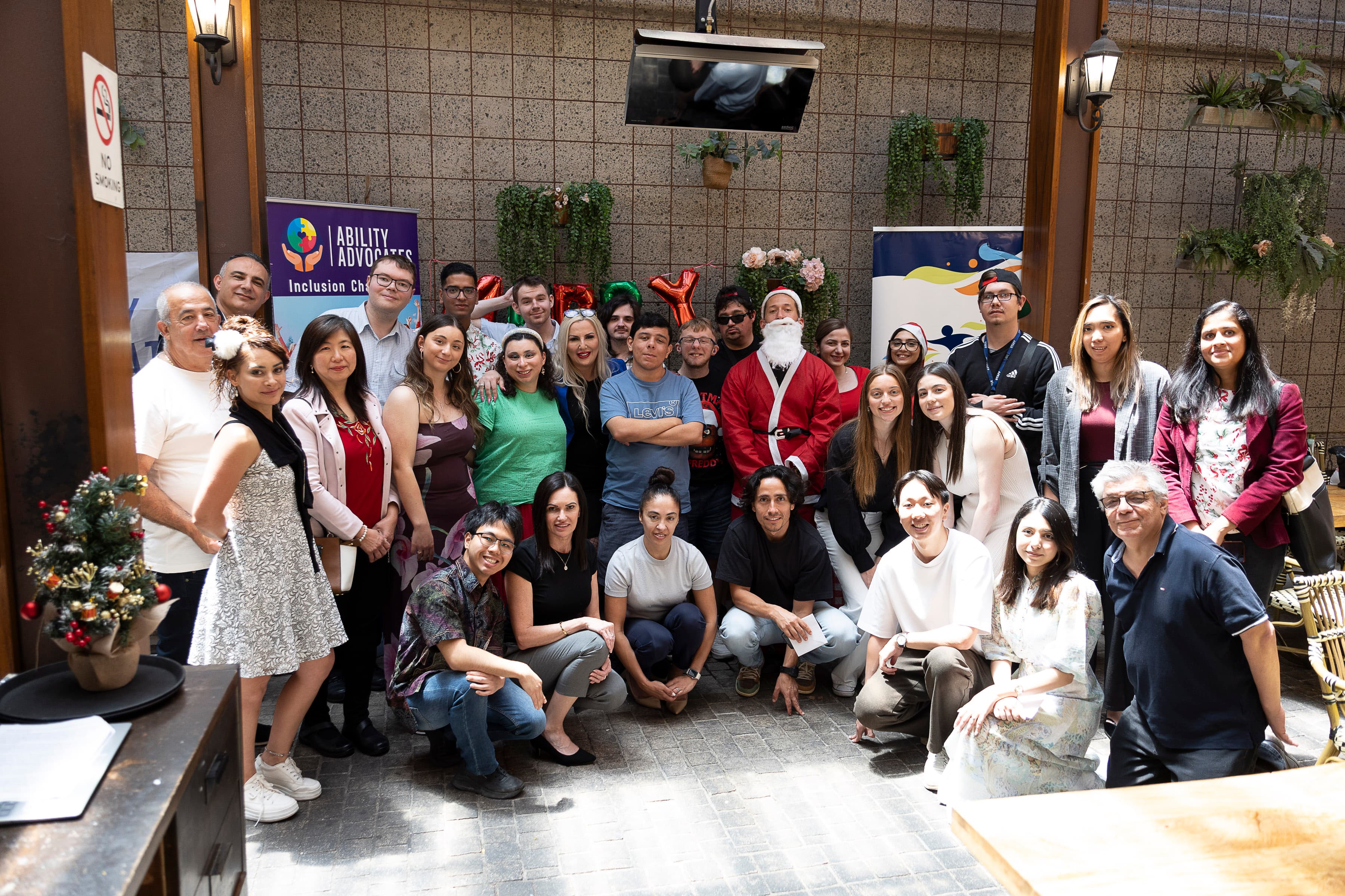 Diverse group of people posing with Santa Claus at an Ability Advocates holiday event.