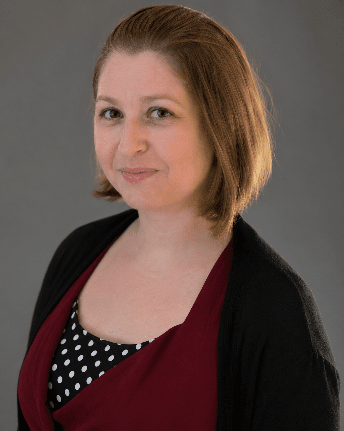 Smiling woman with short brown hair wearing a black cardigan and polka dot shirt.