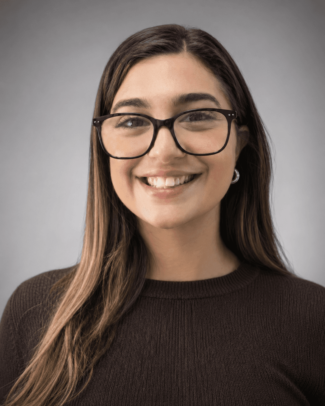 Smiling woman with long brown hair and black-rimmed glasses in a dark brown ribbed sweater.
