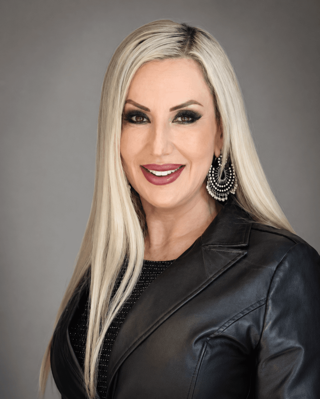 Smiling woman with long blonde hair, dark eye makeup, and a black leather jacket.