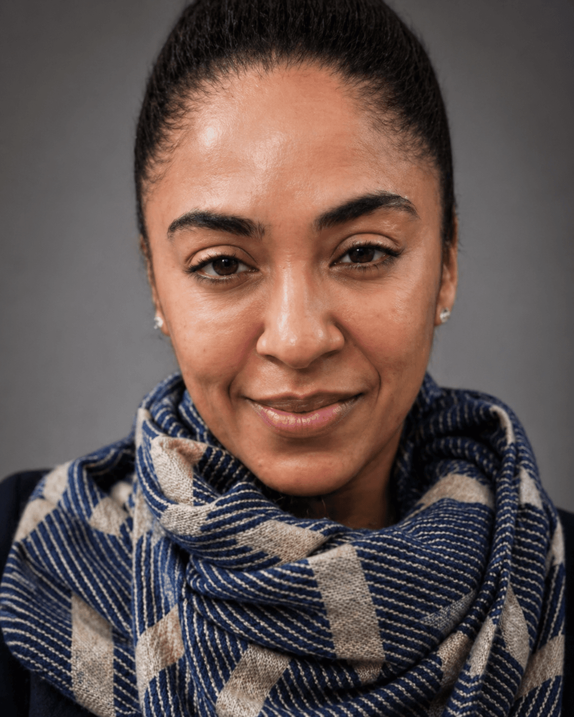 Woman with dark hair pulled back, wearing a blue and beige patterned scarf, smiling gently.