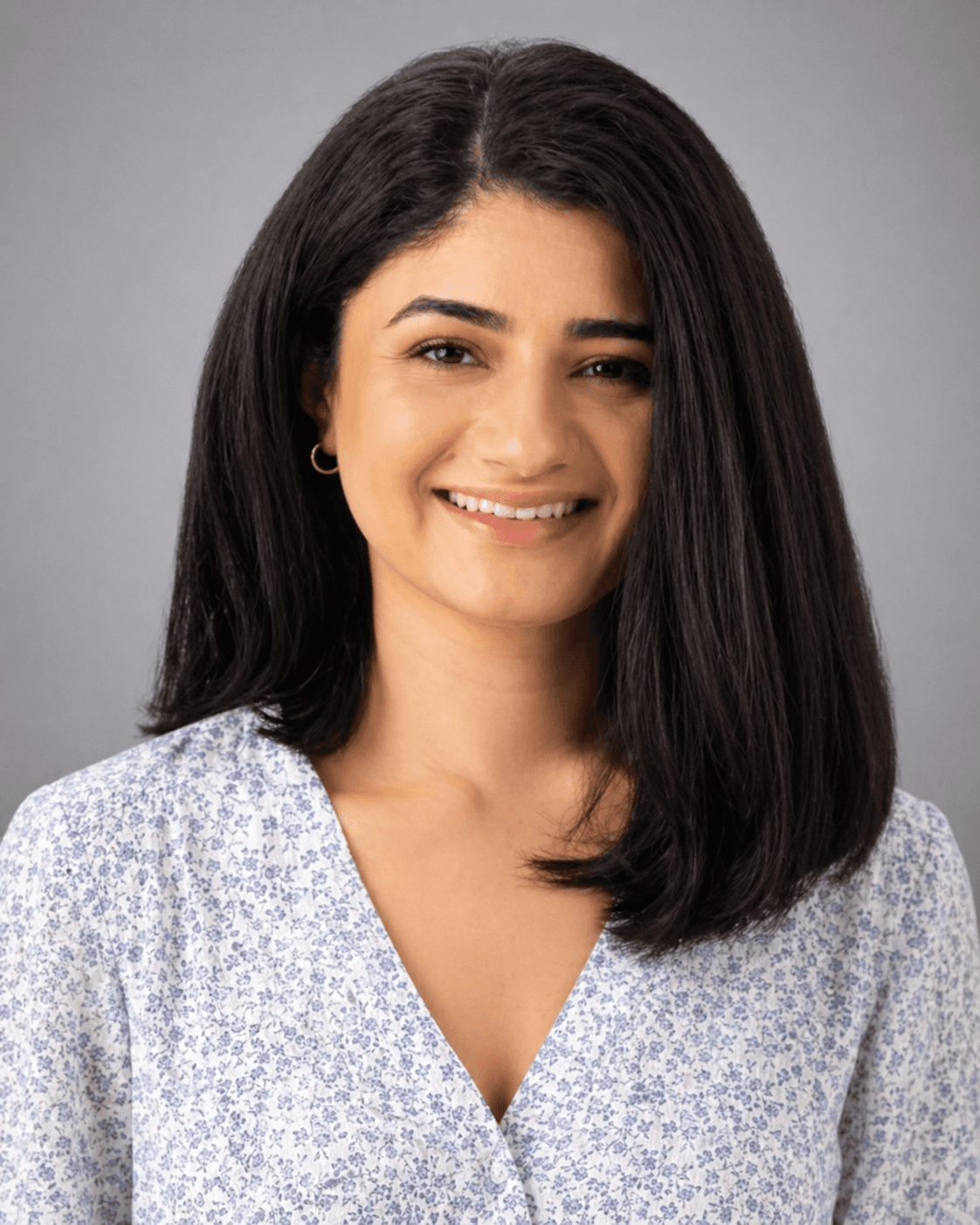 A smiling woman with dark hair wearing a white and blue floral V-neck blouse.